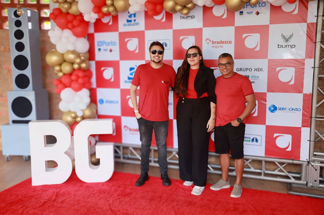 Equipe do Grupo Barra Grande no backdrop do evento, com as letras BG e balões vermelhos e dourados